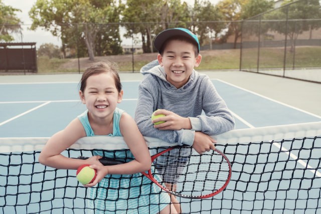 テニスコートのネットにもたれている男の子と女の子