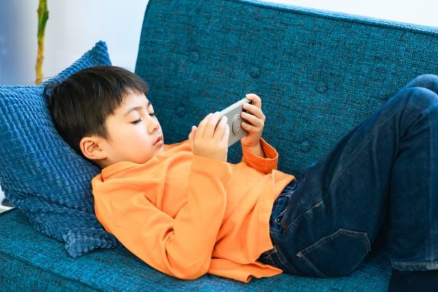 ソファに寝転んでゲームをしている男の子